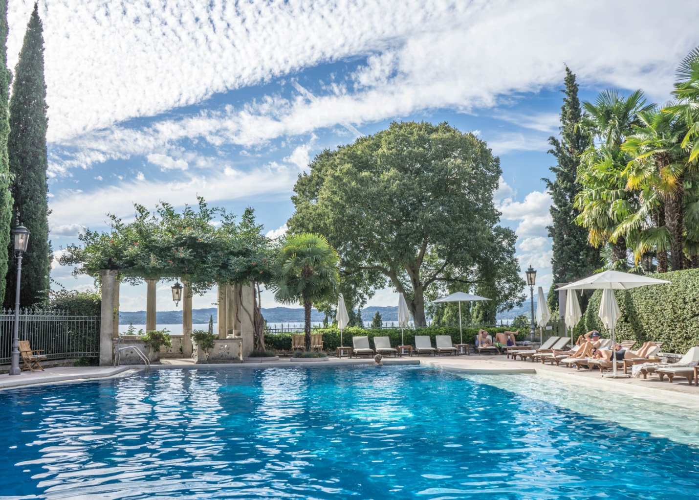 Outdoor living space with a huge pool and foliage with people lounging.