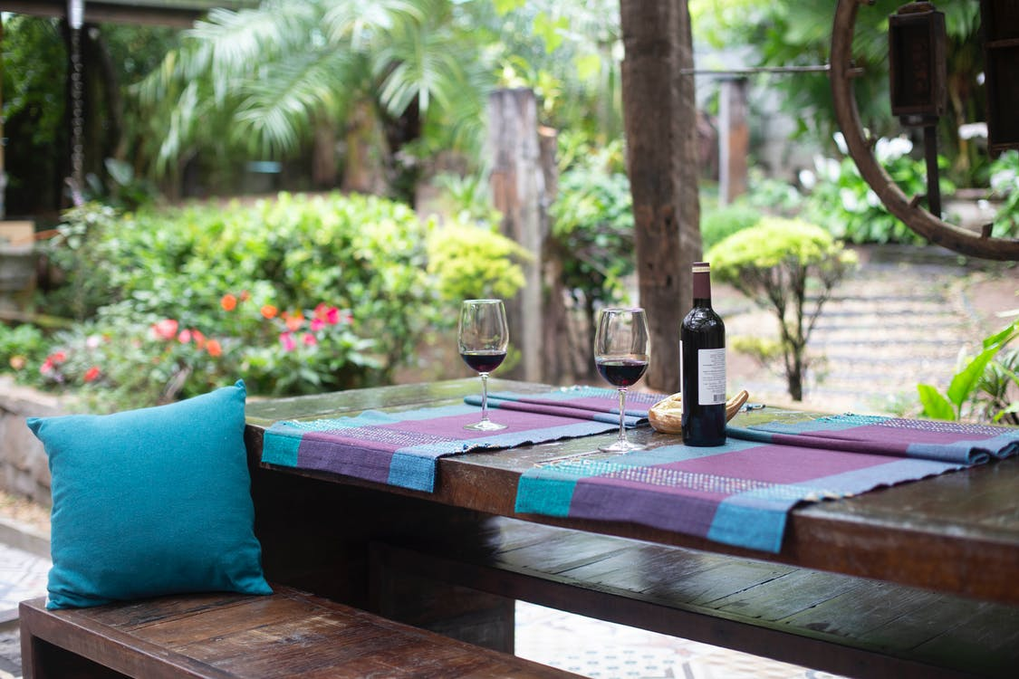 An outdoor space with a table and purple mat cover and a bottle of wine and glasses.