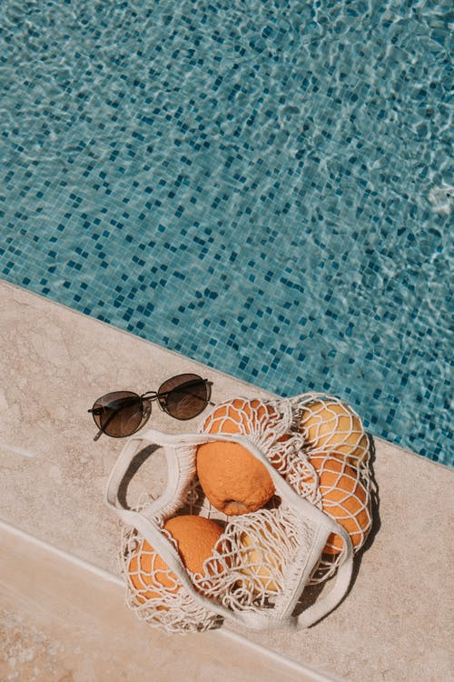 Sunglasses and oranges on waterline stone tiles with a background of mosaic tiles on pool floor