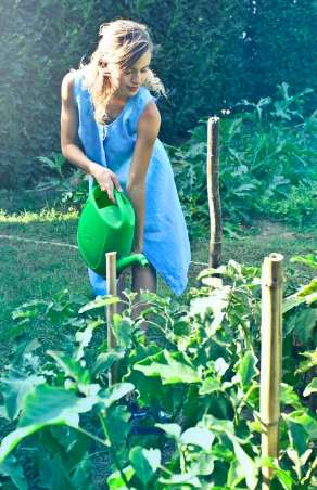 A woman watering greens in her outdoor living space with a water jug