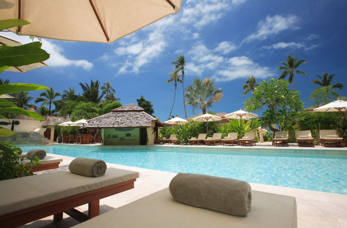 An image of a swimming pool surrounded by chairs and a shade