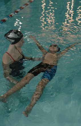 Two people swimming in a pool with protective gear