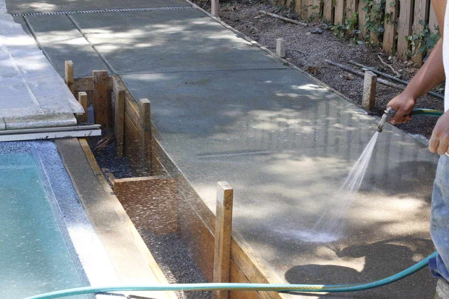 A pool constructor washing the concrete near the pool